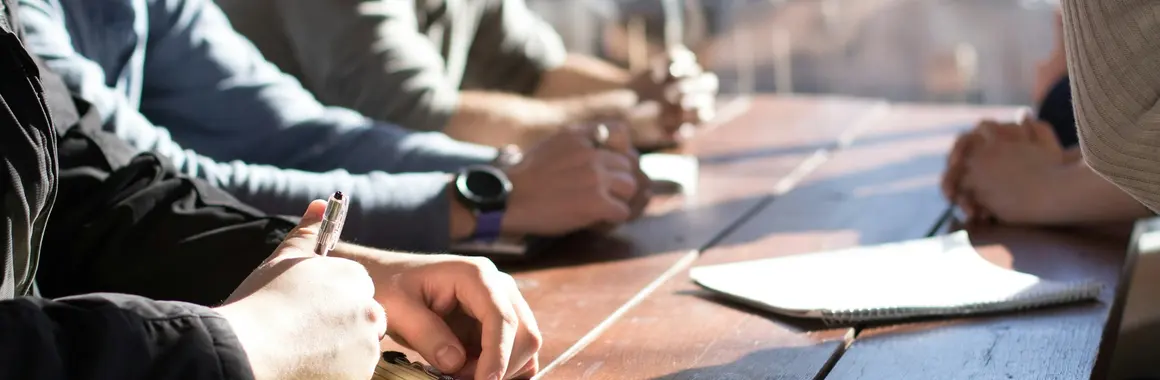 Plusieurs personnes réunies autour d'une table, prenant des notes sur des carnets